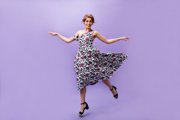 Chica joven en vestido mullido salta sobre fondo morado. Hermosa mujer hermosa en ropa de moda colorida sonriendo sobre fondo aislado.