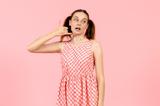 Chica joven en vestido rosa mostrando pose de llamada telefónica en rosa