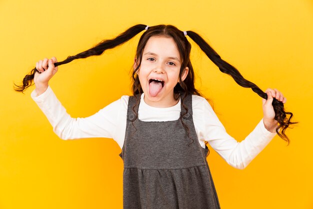 Chica juguetona con la lengua afuera mientras sostiene el cabello de coletas