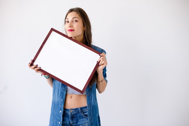 Chica juguetona sostenga un cartel o cartel blanco en blanco