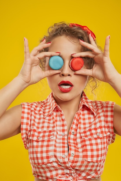 Chica juguetona sosteniendo coloridos macarons haciendo binoculares