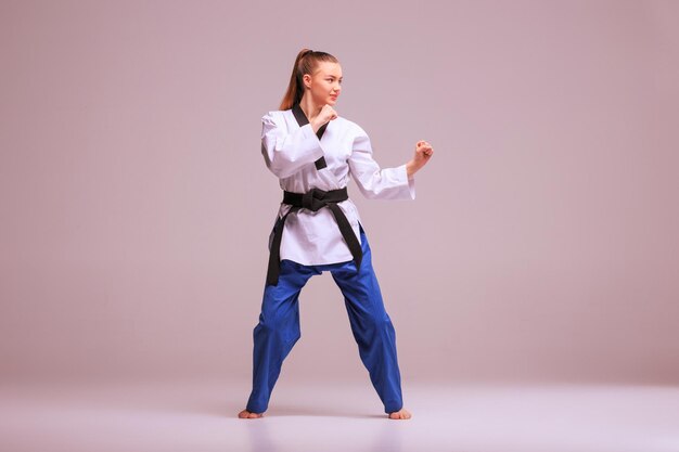 La chica de karate en kimono blanco y karate de entrenamiento de cinturón negro sobre fondo gris.