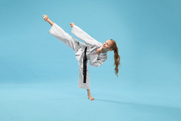 Chica en kimono practicando patada hacia adelante.