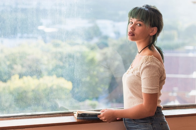 Foto gratuita chica con libro en frente de una ventana