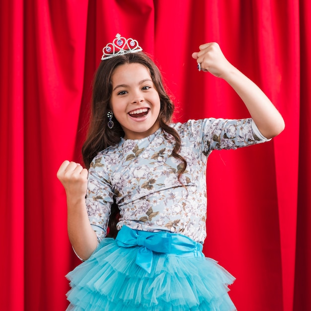 Chica linda alegre haciendo ganador gesto de pie delante de la cortina roja