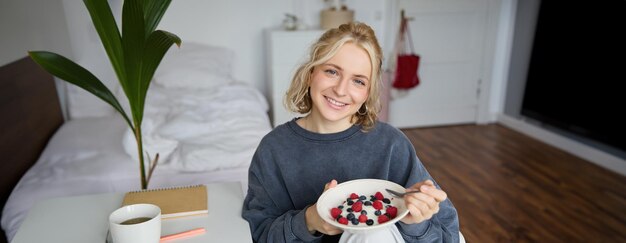 Una chica linda desayuna y bebe té en su habitación se hace un almuerzo saludable en un cuenco se sienta en