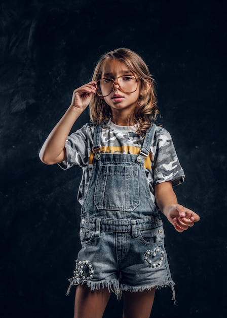 Una chica linda con gafas grandes posa para un fotógrafo en un estudio fotográfico oscuro.