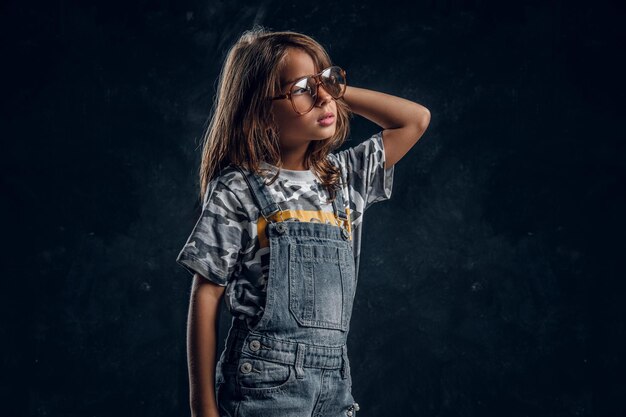 Una chica linda con gafas grandes posa para un fotógrafo en un estudio fotográfico oscuro.