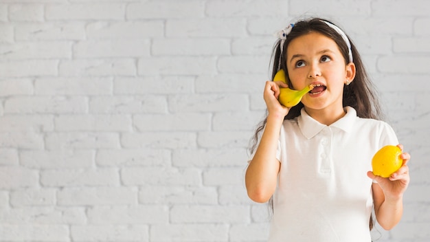 Foto gratuita chica loca sosteniendo el limón en la mano riéndose con plátano amarillo