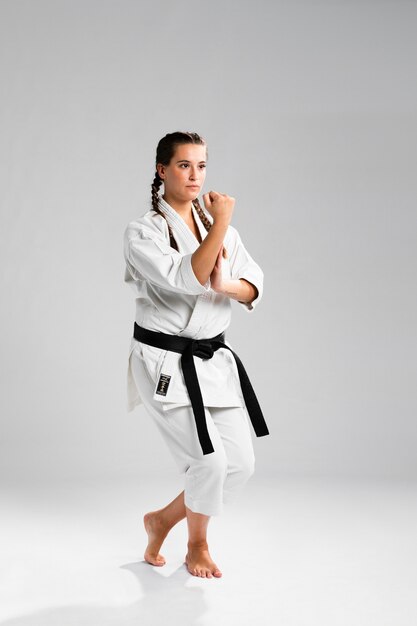 Chica luchadora en posición de combate vistiendo el uniforme blanco sobre fondo gris