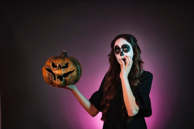 Chica con makeup de halloween sujetando calabaza