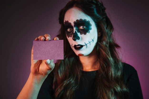 Chica con makeup de halloween sujetando tarjeta de visita