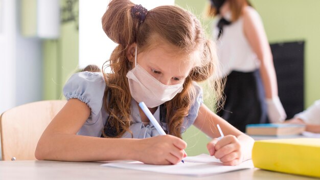 Chica con máscara médica escribiendo una nueva lección