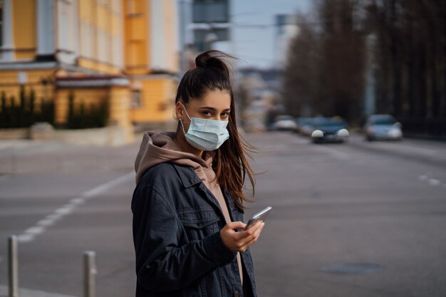 Chica de la máscara protectora con smartphone al aire libre. COVID 19. Pandemia mundial de coronavirus.