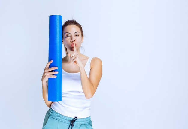 Chica con un mate de yoga azul pidiendo silencio.