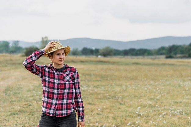 Chica en una mierda cuadrada roja sosteniendo su sombrero en el campo