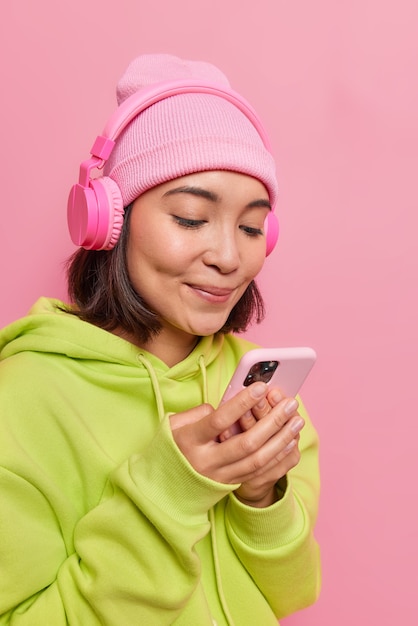 Chica mira atentamente la pantalla del teléfono inteligente escucha la pista de audio en auriculares vestidos casualmente de rosa siendo adicto a las tecnologías modernas