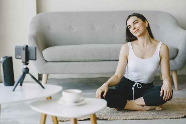 Chica mira el teléfono. Yogi amasando. Mujer en casa en ropa deportiva.