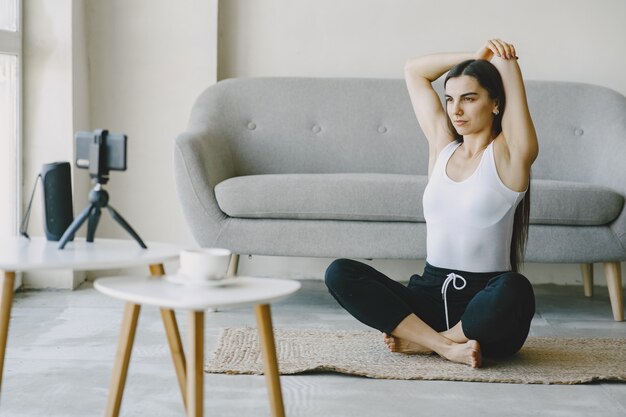 Chica mira el teléfono. Yogi amasando. Mujer en casa en ropa deportiva.