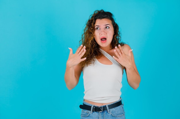 Chica mirando hacia arriba está tomados de la mano cerca del pecho sobre fondo azul.