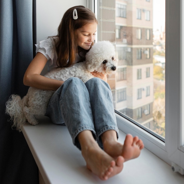 Chica mirando por la ventana con su perro en casa