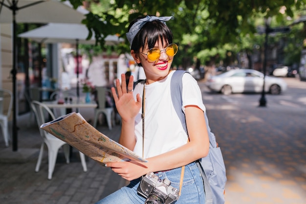 Chica de moda alegre agitando la mano en el anillo de plata y sonriendo, mirando a otro lado