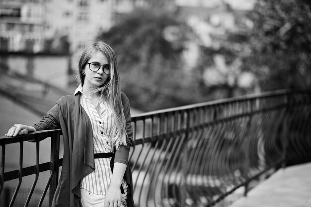 Chica de moda con gafas y jeans rotos contra la barrera en la calle