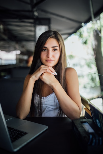 Chica modelo bastante seria trabaja en su computadora portátil en la terraza del café daytilme