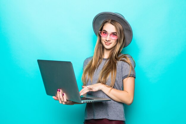 Chica modelo de estudiante sonriente en ropa casual de moda trabaja relojes en su computadora portátil aislada en verde