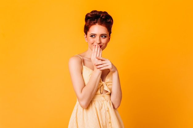 Chica modelo sonriendo y cubriendo la boca con las manos. Foto de estudio de alegre mujer jengibre con peinado elegante.