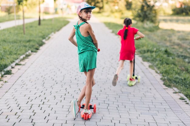 Chica montando en scooter con su amiga en la pasarela del parque