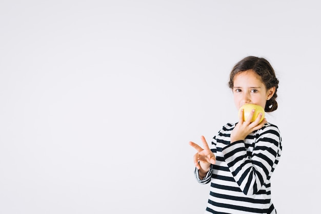 Chica mordiendo la manzana y gesticulando la paz