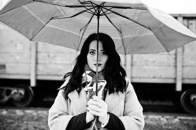 Foto gratuita chica morena en abrigo gris con paraguas rojo en la estación de tren