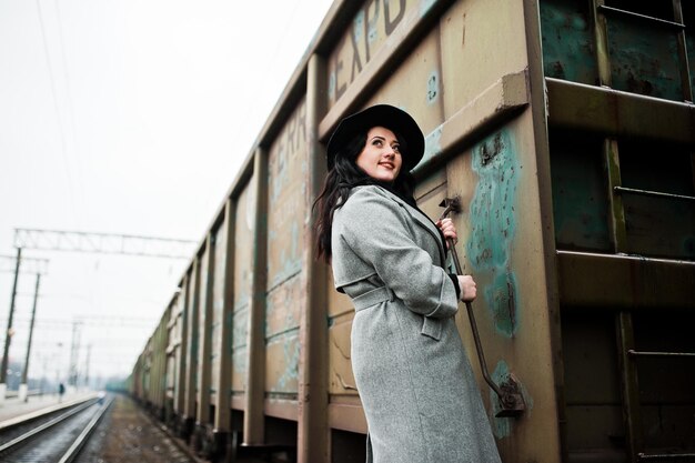 Chica morena con abrigo gris con sombrero en la estación de tren