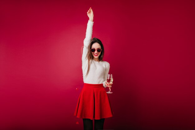 Chica morena bien formada en falda roja celebrando algo con champán