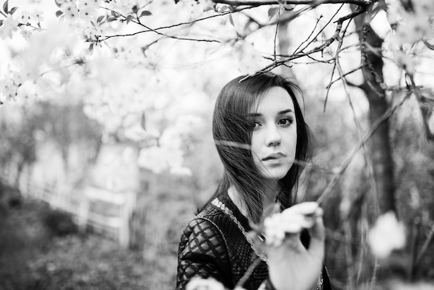Chica morena con la cara fija en la chaqueta de cuero posada en el jardín de primavera Fotografía en blanco y negro