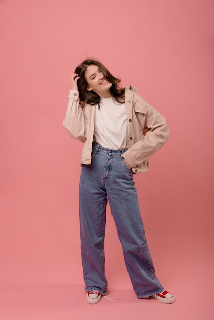 Chica morena caucásica joven con estilo de cuerpo entero viste chaqueta de camiseta y jeans sobre fondo rosa Concepto de belleza femenina de estilo de vida