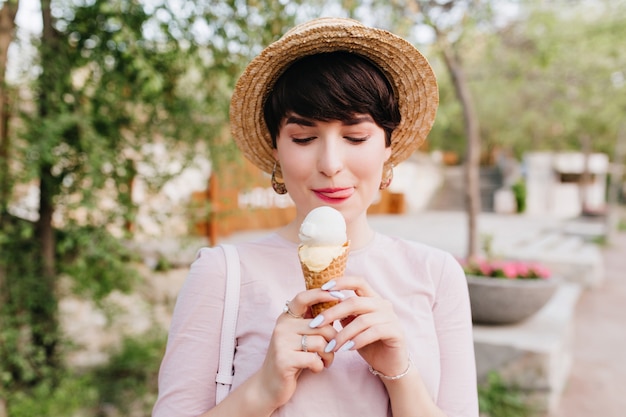 Chica morena complacida en ropa de moda se lame el labio mirando un postre delicioso