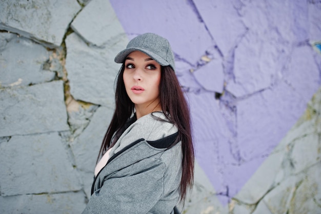 Chica morena con estilo en gorra gris estilo casual de la calle en el día de invierno contra la pared de color