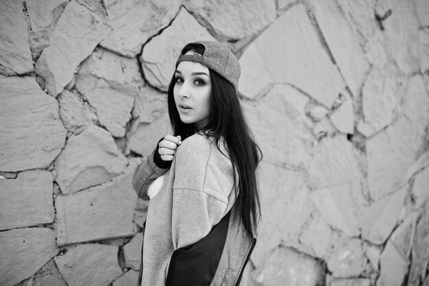 Chica morena con estilo en gorra gris estilo casual de la calle en el día de invierno contra la pared de color