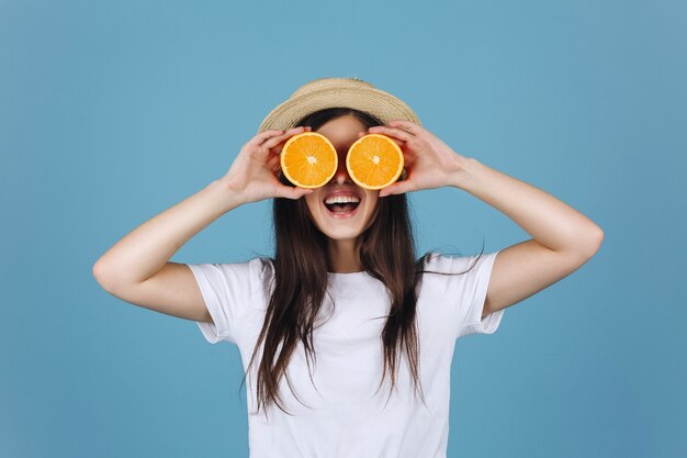 Chica morena con falda amarilla sostiene naranjas ante sus ojos y sonríe