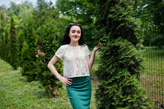 Chica morena con falda verde y blusa blanca posada en el parque