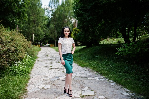 Chica morena con falda verde y blusa blanca posada en el parque