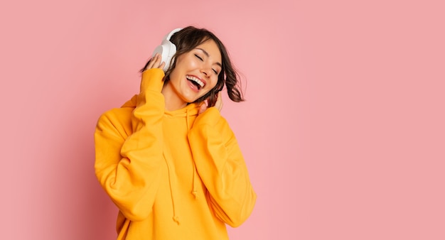 Chica morena feliz escuchando música y bailando en rosa. El uso de sudadera con capucha naranja.