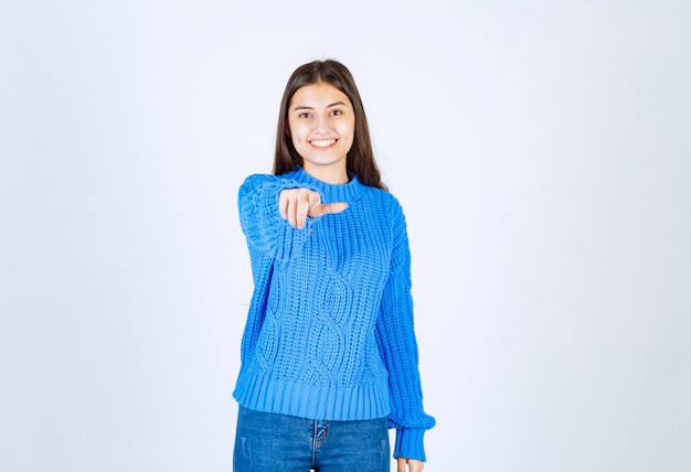 Chica morena joven en suéter azul apuntando hacia adelante en blanco.