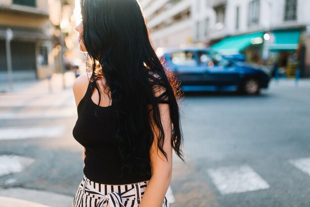 Chica morena de pelo largo en camiseta negra caminando por la calle explorando la ciudad nueva en algún lugar de Europa