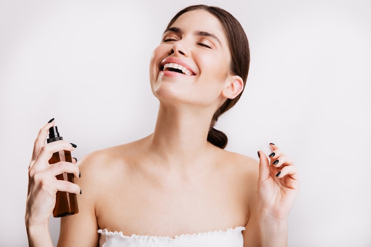 Foto gratuito chica morena satisfecha después de la ducha rocía niebla para el cuerpo en la piel. mujer sonriendo en la pared aislada.