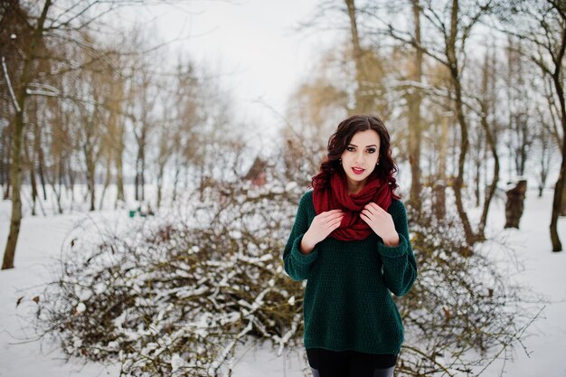 Chica morena en suéter verde y bufanda roja al aire libre en el día de invierno por la noche