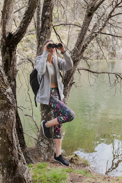 Foto gratuita chica morena usando prismáticos apoyada en un árbol