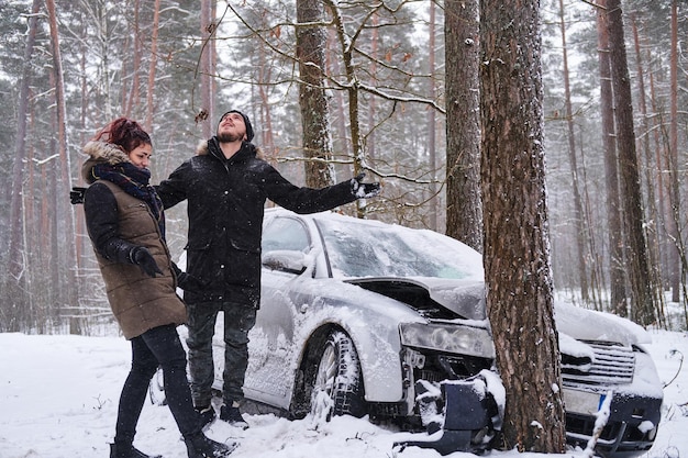 La chica le muestra a su novio los daños a su auto después del accidente. La niña estrelló el auto de su novio. Coche estrellado tras accidente en bosque nevado